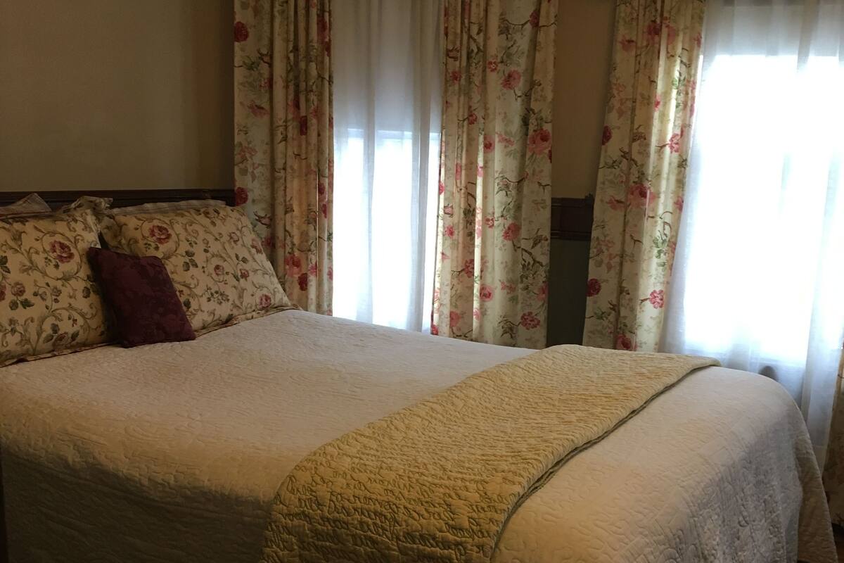 A bedroom with a large bed, floral curtains, and a wooden floor.