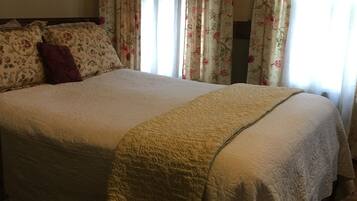 Un dormitorio con una cama grande, cortinas con motivos florales y suelo de madera.