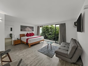 Una habitación de hotel moderna con una cama, un sofá, una mesita y un balcón con vistas a zonas verdes.