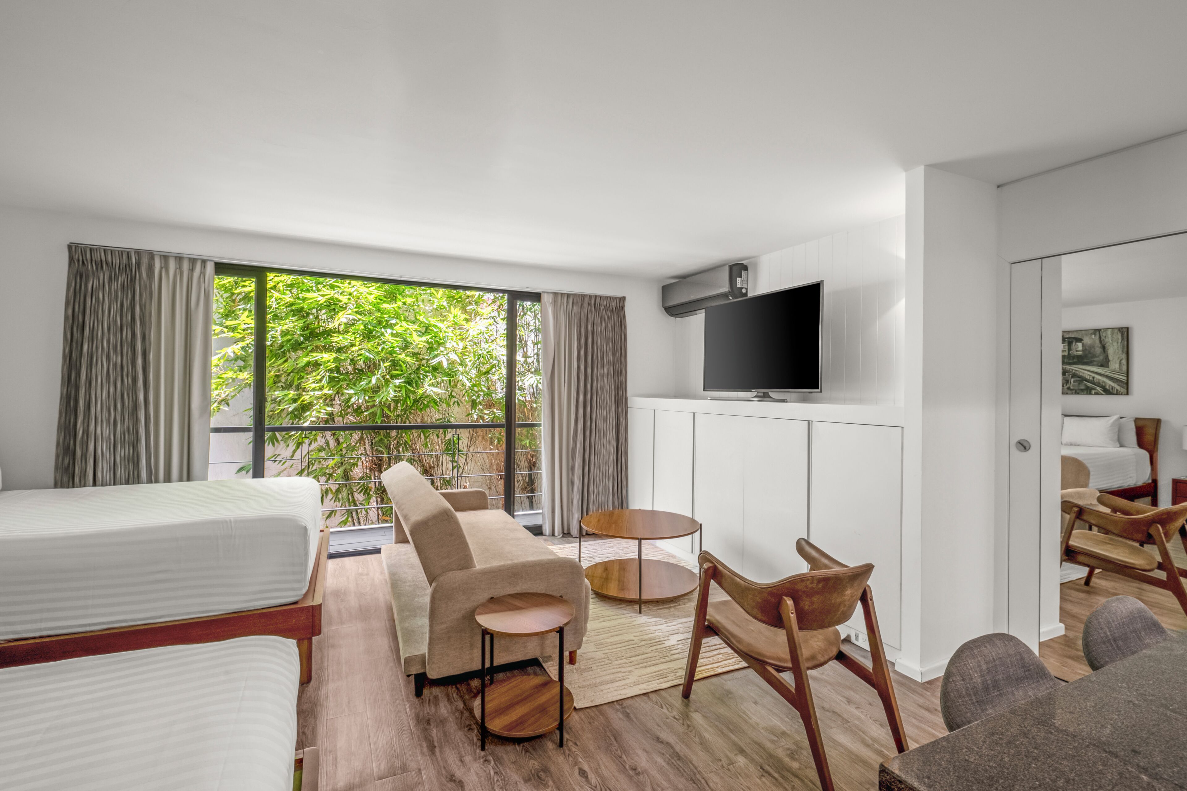 Ein modernes Hotelzimmer mit Bett, Sofa, Stühlen, einem Fernseher und Blick auf Grünflächen.