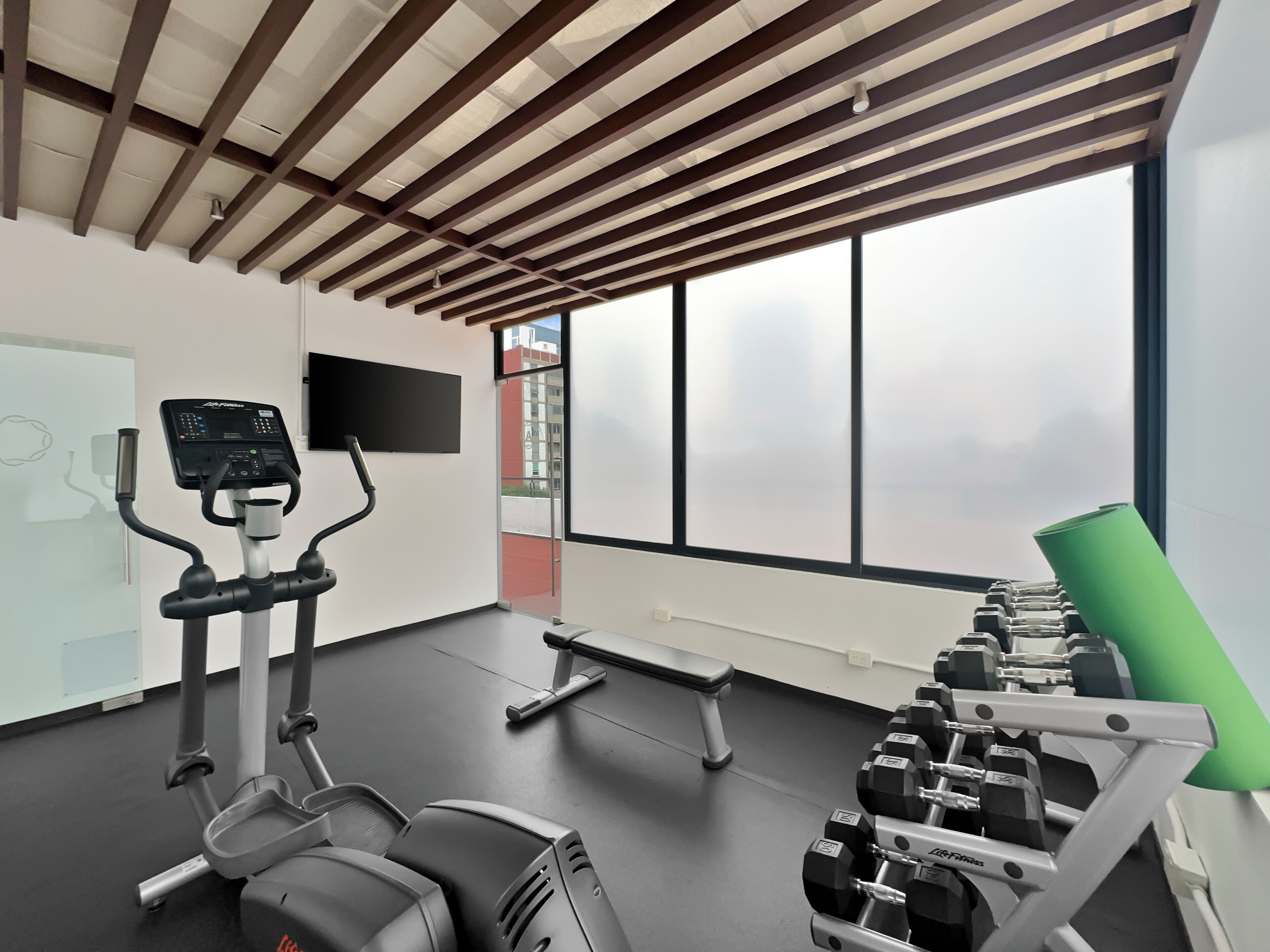 A gym with exercise equipment, a bench, and large windows.