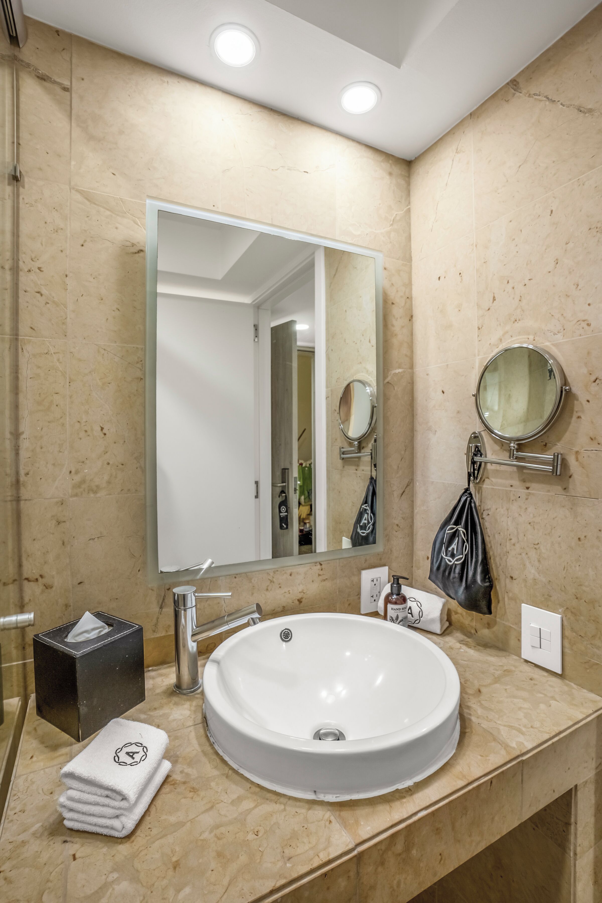 Un baño con un espejo grande, un lavabo redondo, una toalla y un dispensador de jabón.