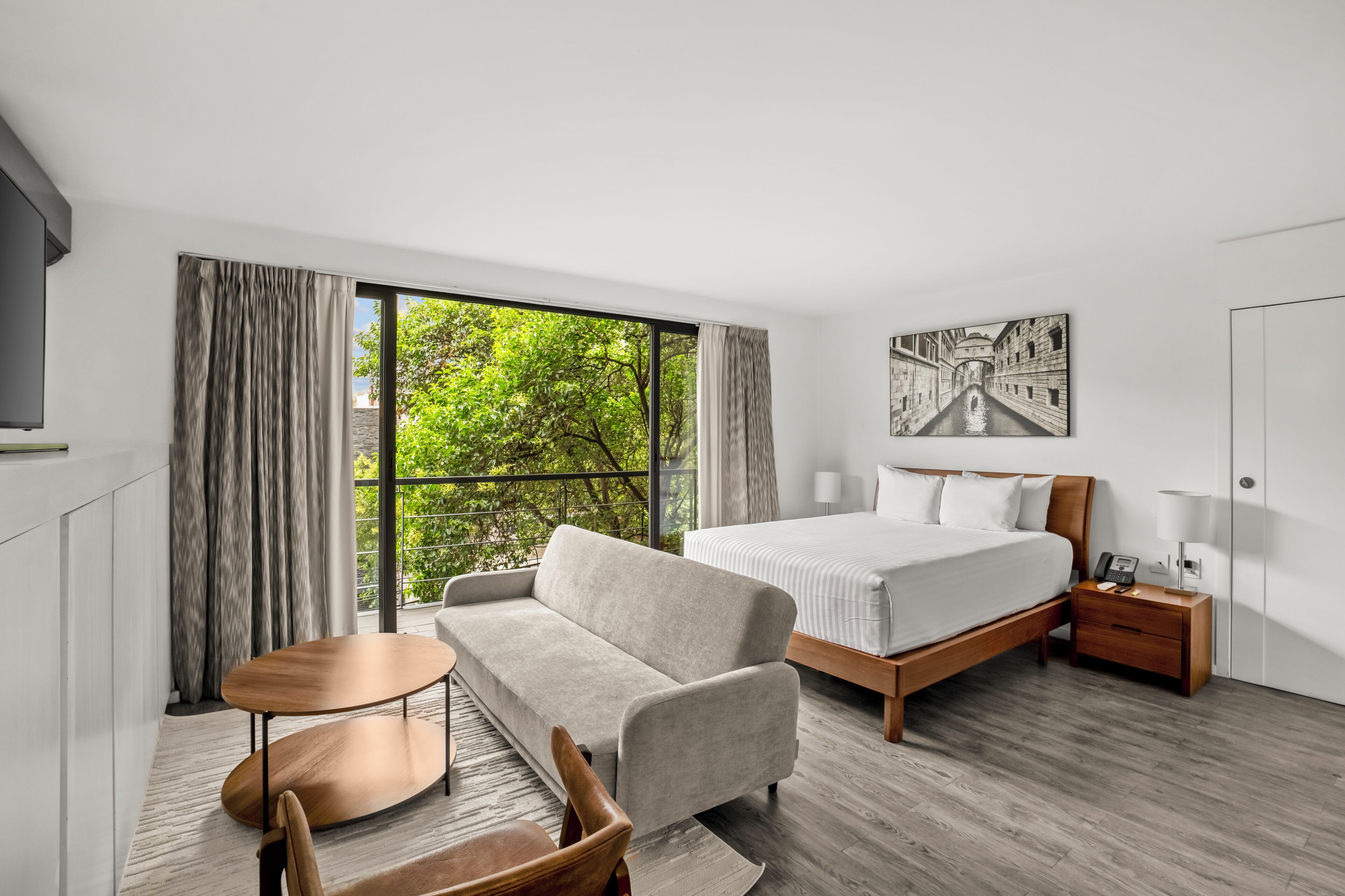 A modern hotel room with a bed, sofa, and a small table.