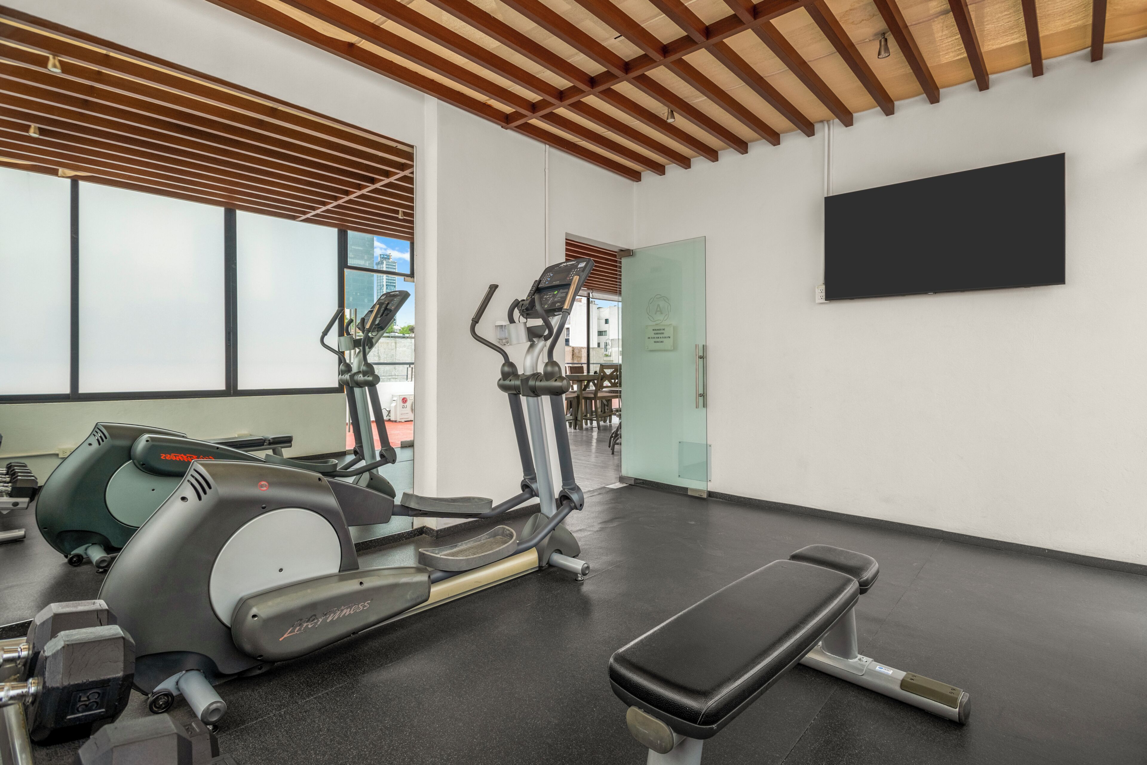 A gym with exercise equipment, a bench, and a large window.