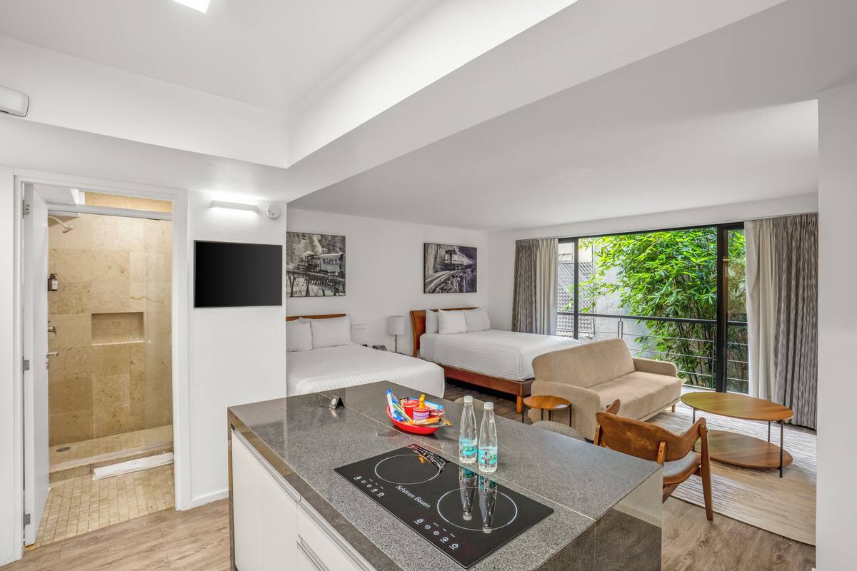 A modern hotel room with a kitchenette, a bed, a sofa, and a balcony with a view.