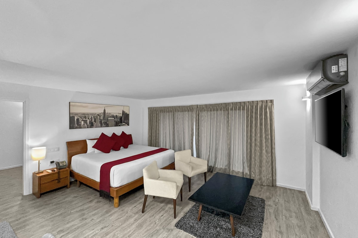 A hotel room with a bed, bedside table, lamp, chair, desk, and a TV mounted on the wall.