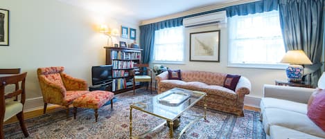 Ein Wohnzimmer mit einer Couch, Sesseln, einem Couchtisch, einem Bücherregal und einem Fernseher.