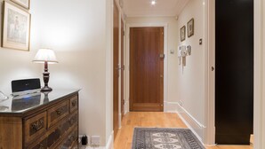 A hallway with a wooden dresser, a lamp, framed pictures, a door, and a patterned rug.