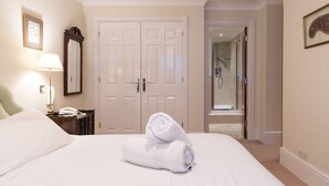 A hotel room with a bed, a nightstand with a lamp, a mirror, a door, and a bathroom visible through an open door.