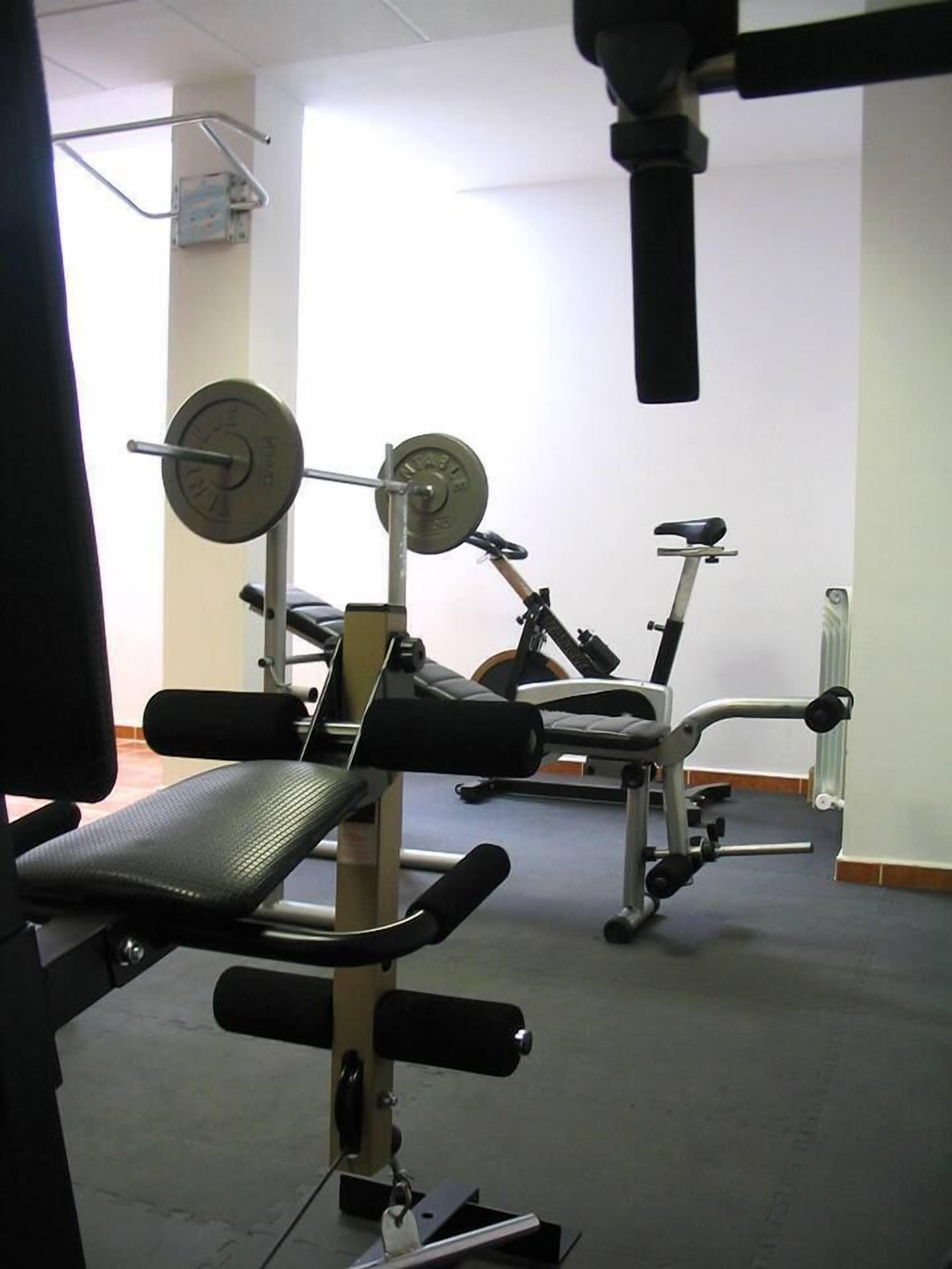 A gym with weightlifting equipment, a stationary bike, and a bench.