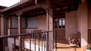 Ein überdachter Außenbereich mit Holzbalkon, Terrakottafliesen und einem hölzernen Wagenrad.