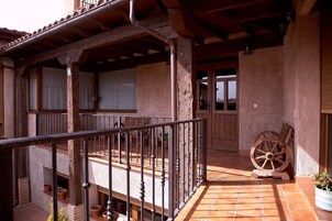 Un espacio al aire libre cubierto con un balcón de madera, baldosas de terracota y una rueda de madera.