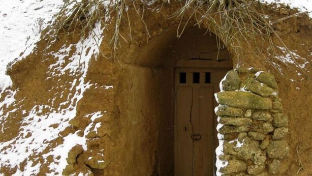 Eine traditionelle Steinhütte mit Holztür und einem Reetdach.