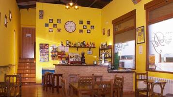 A restaurant with yellow walls, wooden furniture, a bar area, and a clock on the wall.