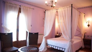 Ein Schlafzimmer mit einem Himmelbett, zwei Korbsesseln, einem runden Tisch und einem Nachttisch mit Lampe.