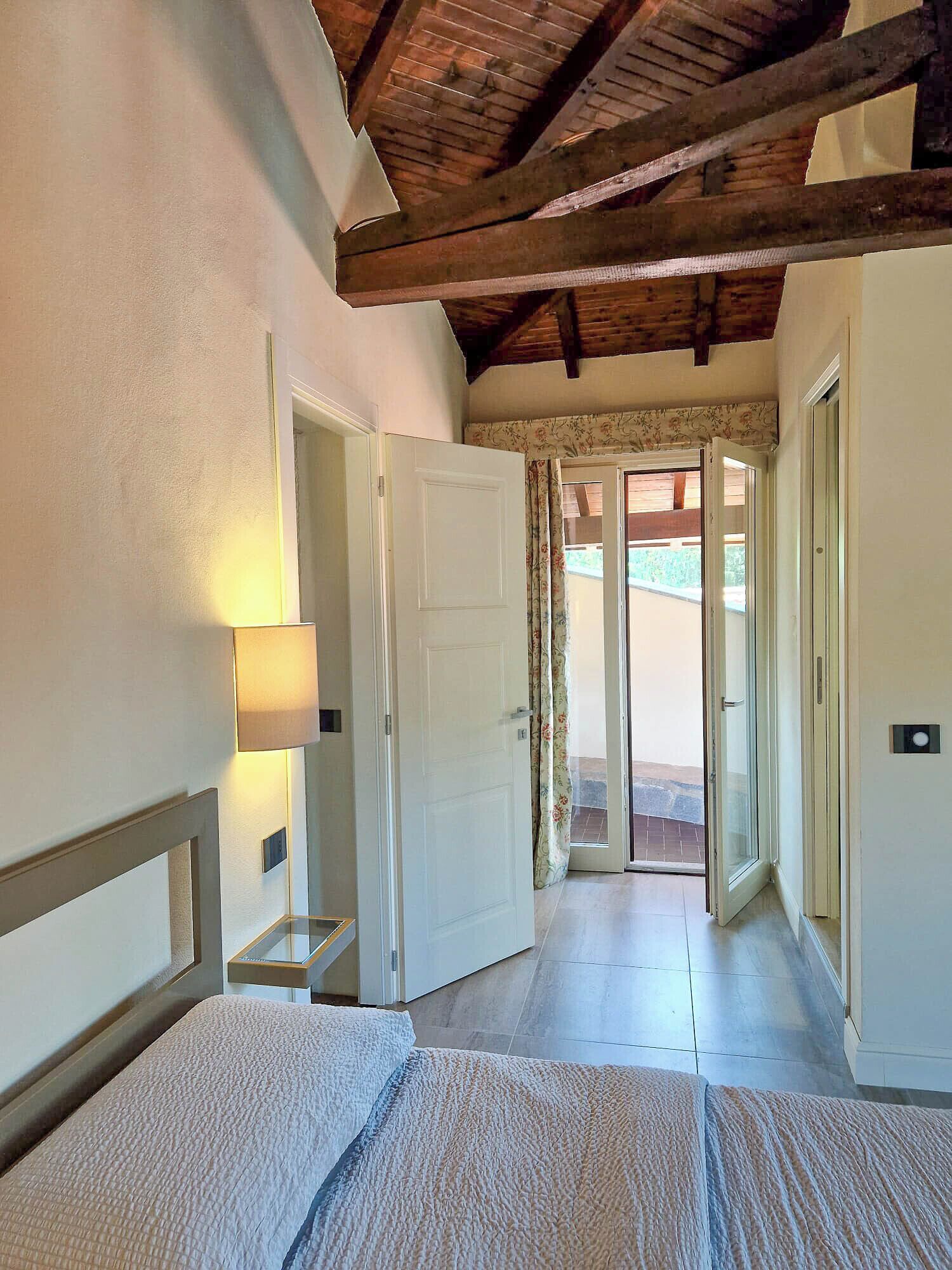 A bedroom with a bed, a nightstand, a lamp, and a wooden ceiling.
