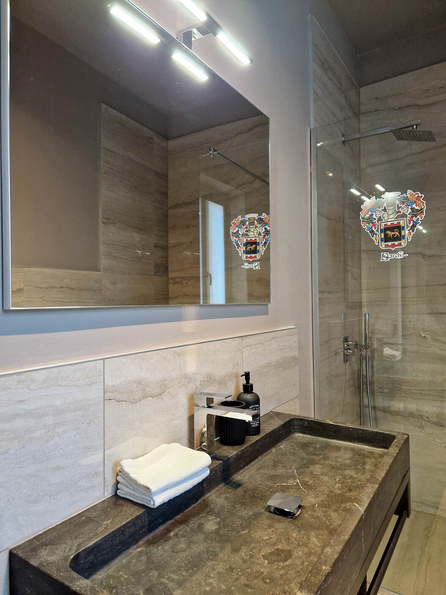 Un baño moderno con un espejo grande, cabina de ducha de vidrio y encimera de mármol.