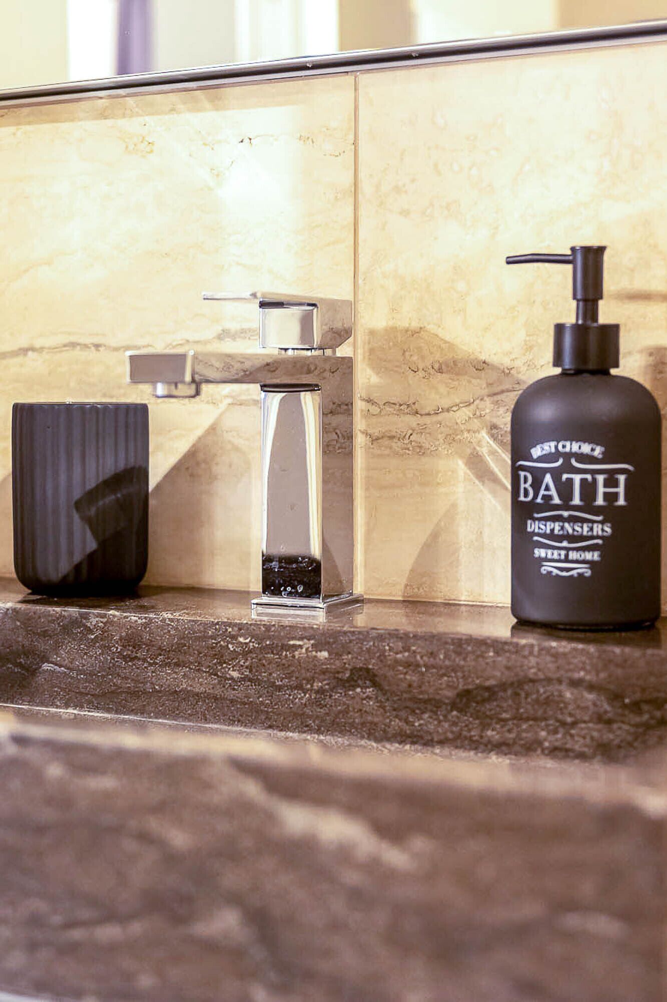 A bathroom vanity with a modern faucet, a soap dispenser, and a black soap bottle.