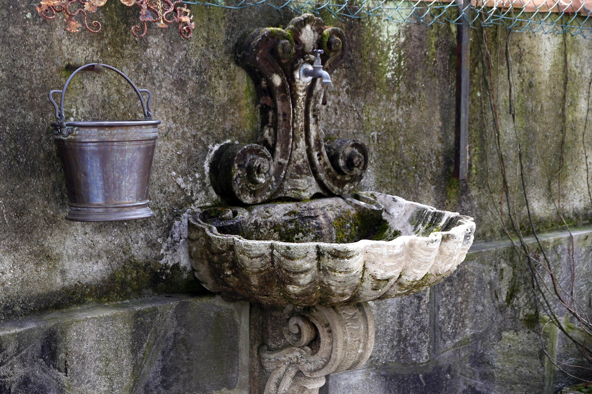 A stone fountain with a metal bucket attached to a wall.