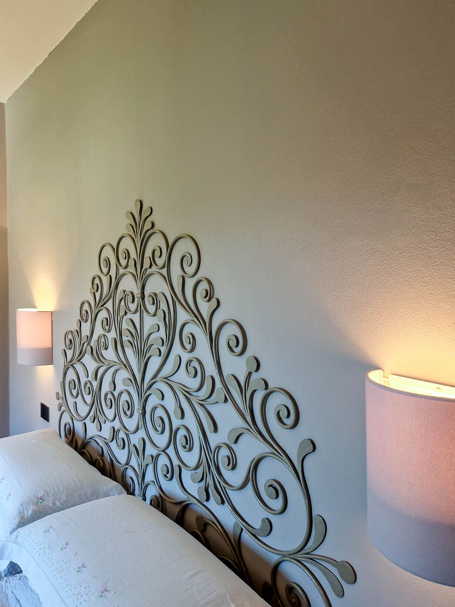 A neatly made bed with a decorative metal headboard, a bedside lamp, and a wall-mounted lamp.