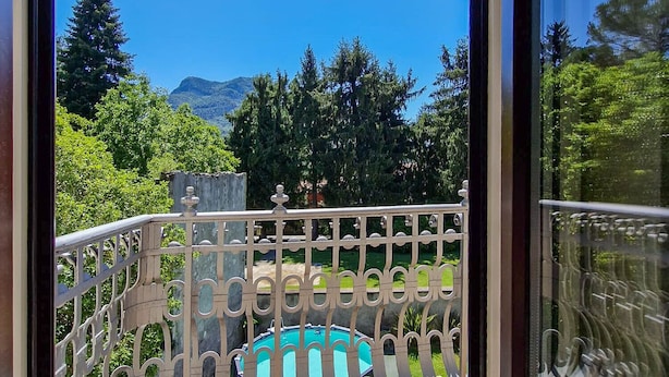 Un balcon avec une piscine, entouré de verdure et avec des montagnes en arrière-plan.