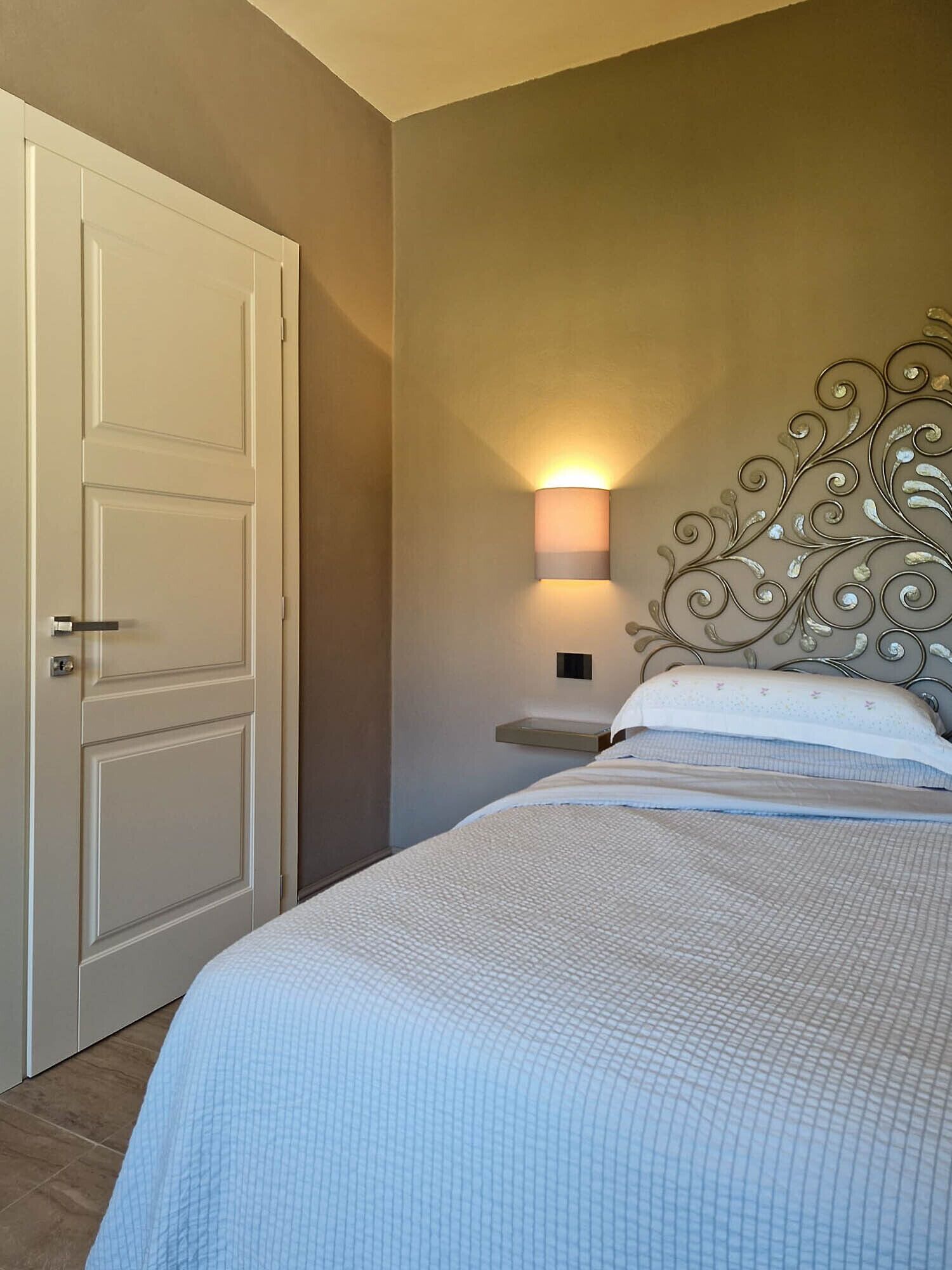 Un dormitorio con cama, mesita de noche, lámpara de pared y una puerta.