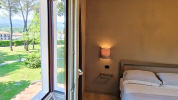 A hotel room with a large window, a bed, a bedside table with a lamp, and a radiator.