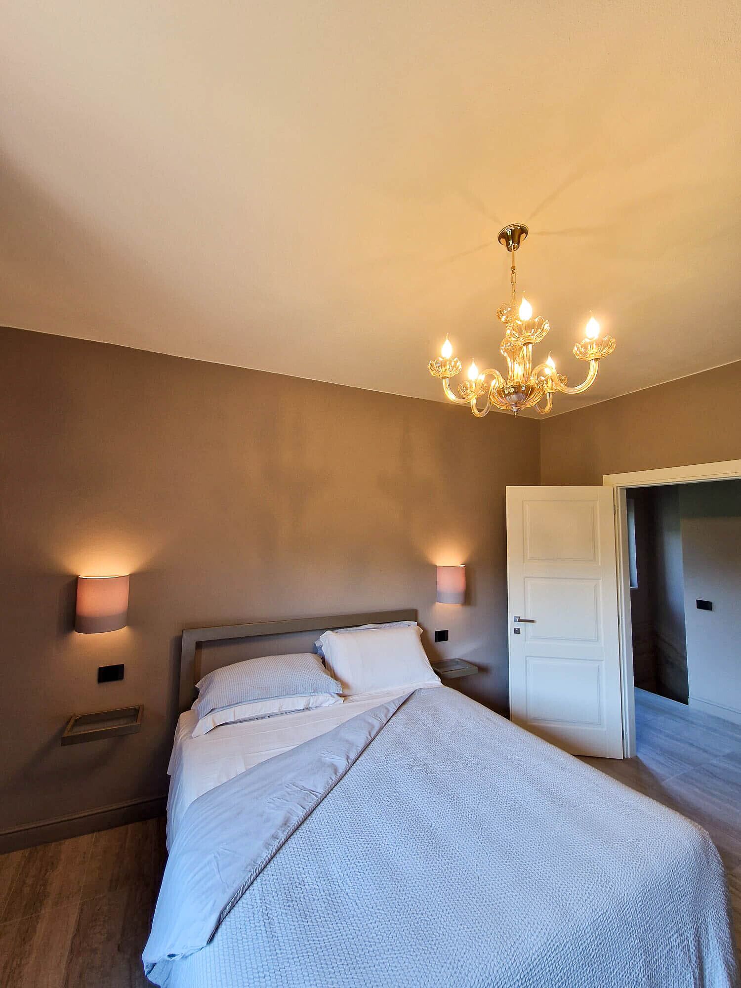 Ein Schlafzimmer mit einem Bett, einer Kristallleuchtre, zwei Wandlampen und einer Tür.