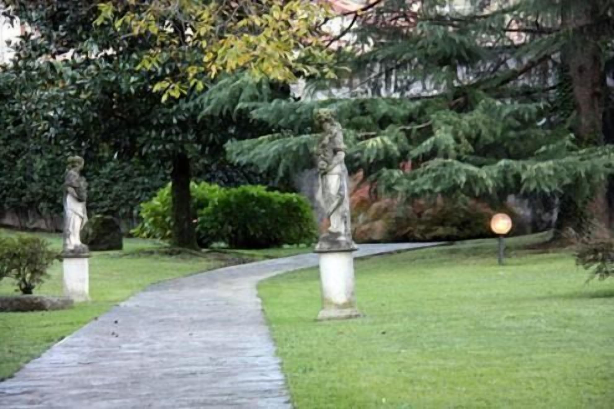 A pathway leading through a garden with statues and a lamppost.