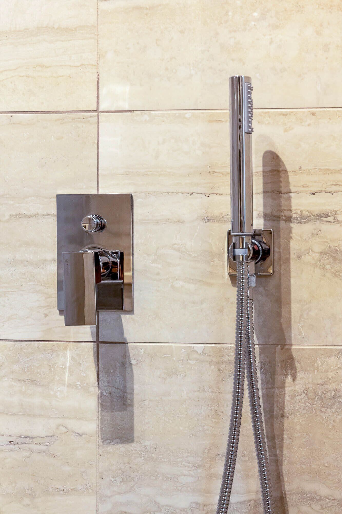 A shower with a handheld showerhead and a wall-mounted control panel.