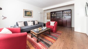 A living room with a dark sofa, red armchairs, a coffee table, and a bookshelf.