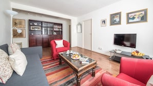A living room with a sofa, red armchair, coffee table, bookshelf, TV, and artwork on the wall.