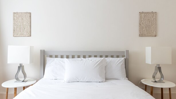 A neatly made bed with white linens, two bedside tables with lamps, and two wall-mounted decorative items.
