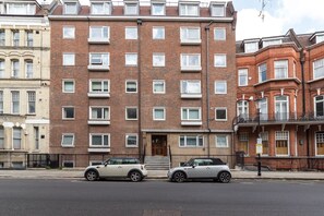 Un immeuble en briques de plusieurs étages, doté d’une entrée centrale et d’un petit escalier menant à cette entrée.