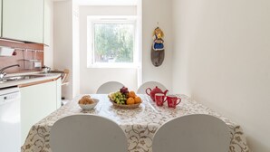 A dining area with a table set for two, a fruit bowl, a teapot, and a red mug.