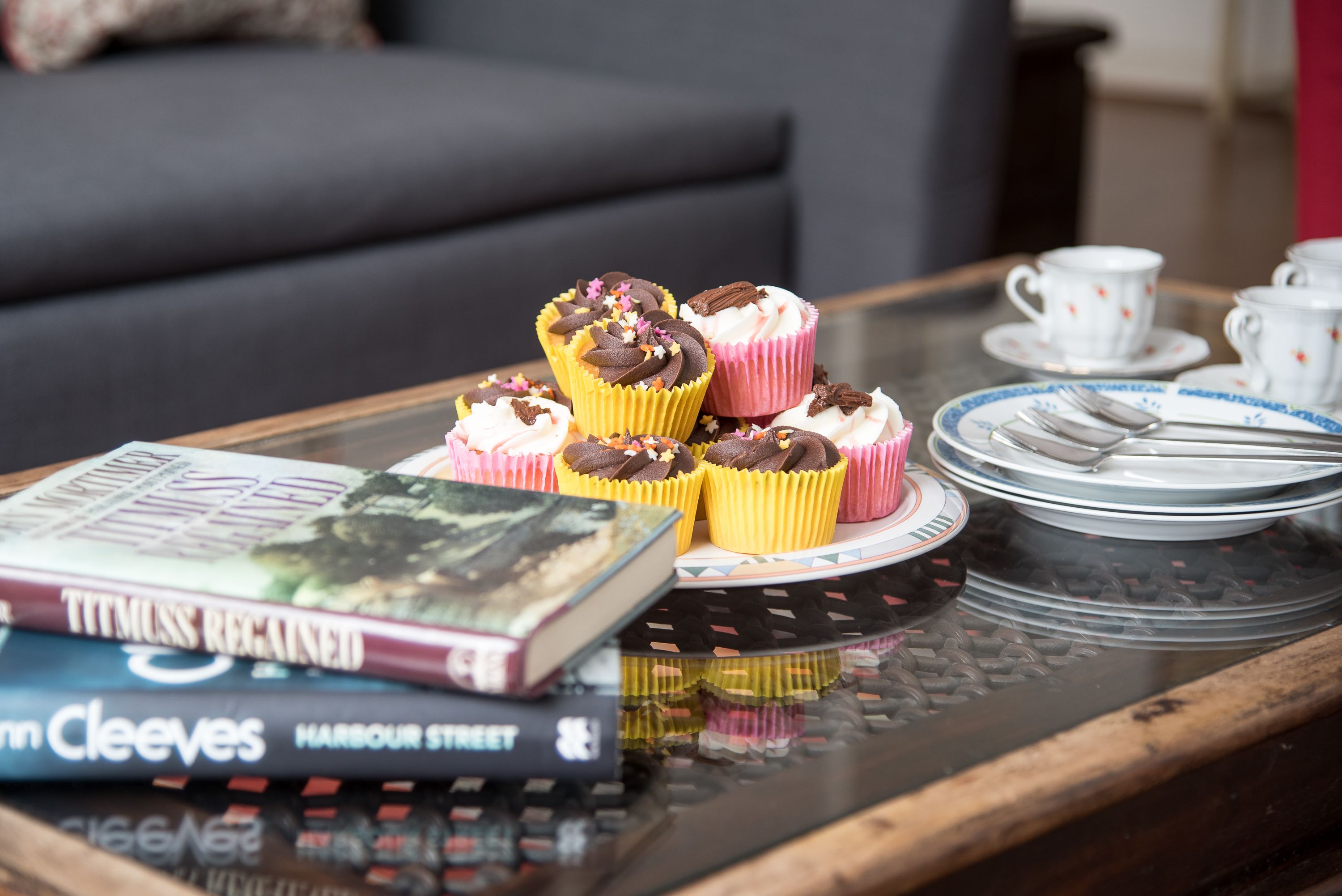 A table with a stack of books, a tray with cupcakes, and a set of white cups and saucers.