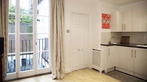 A modern kitchen with white cabinets, a black countertop, and a sliding glass door leading to a balcony. - A Place Like Home - Inviting Flat near South Kensington (London)