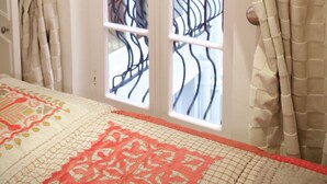 A bedroom with a bed, beige curtains, a window with a balcony, and a door. - A Place Like Home - Inviting Flat near South Kensington (London)