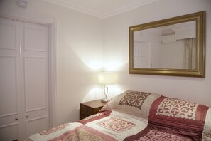 Ein Schlafzimmer mit Bett, Nachttisch, Lampe, Spiegel und Tür.