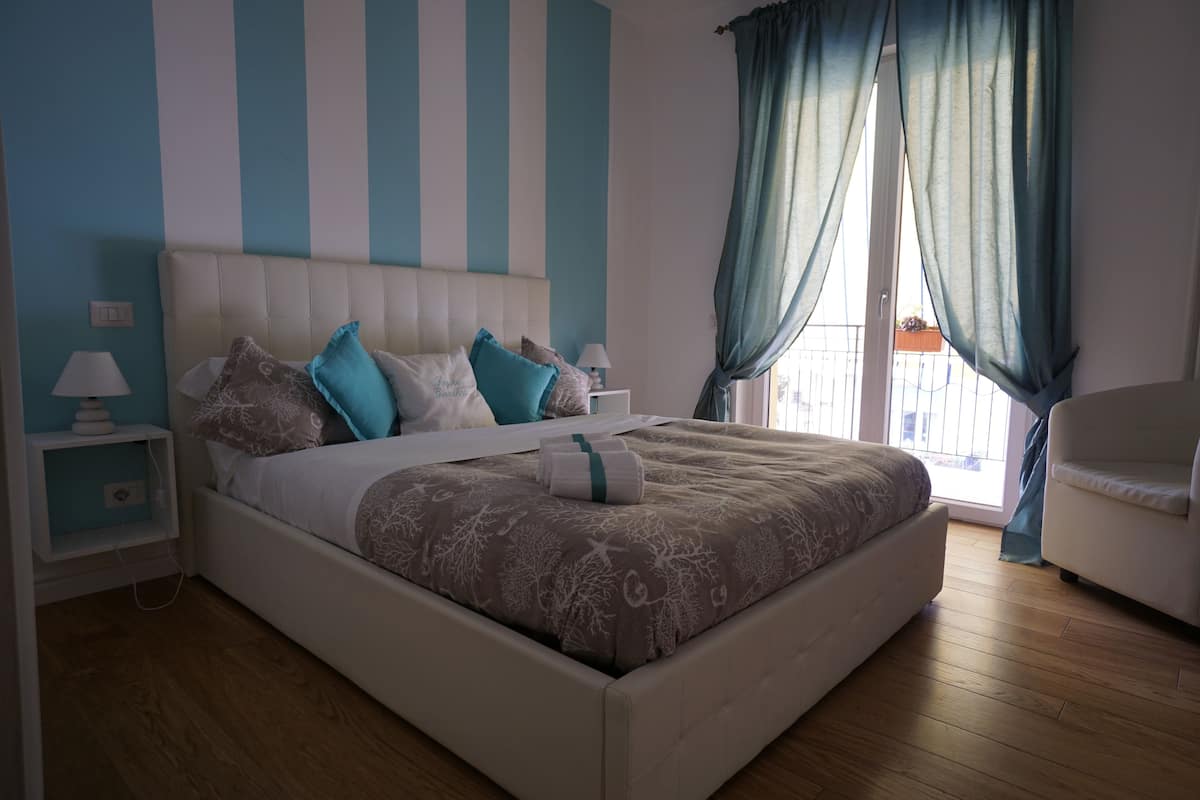 A bedroom with a large bed, a nightstand, a chair, and a view of the outside.