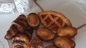 Ein Tisch mit einer Auswahl an Gebäck, darunter Croissants und ein Kuchen, sowie einem Glas Wasser.