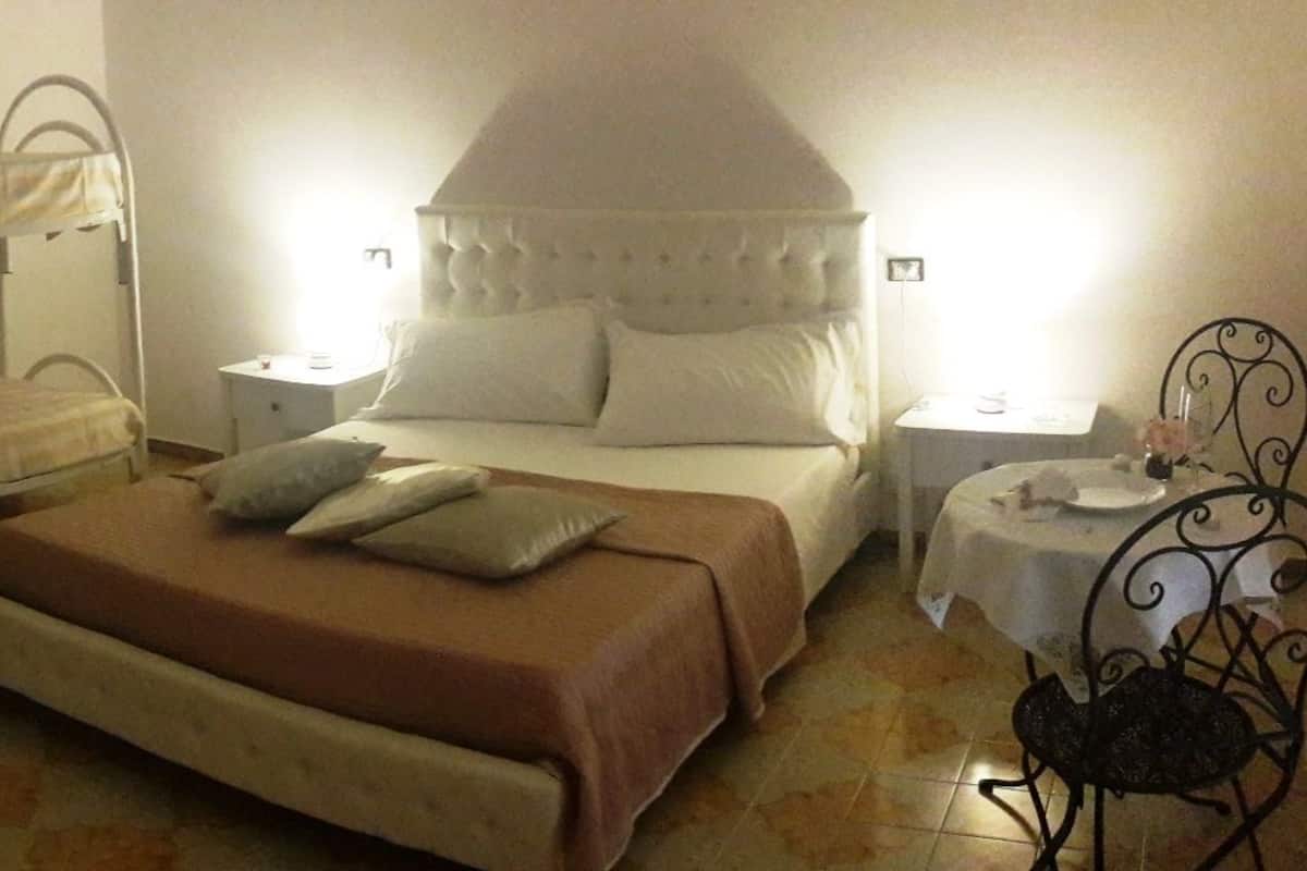 Un dormitorio con una cama litera, una cama individual, una mesita de noche con una lámpara y una pequeña mesa con un florero.