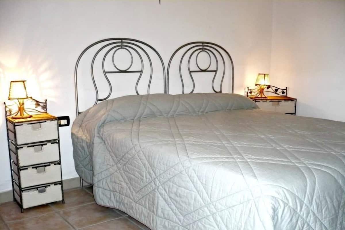 Un letto con un piumone bianco trapuntato, due comodini con lampade e una testiera in metallo.
