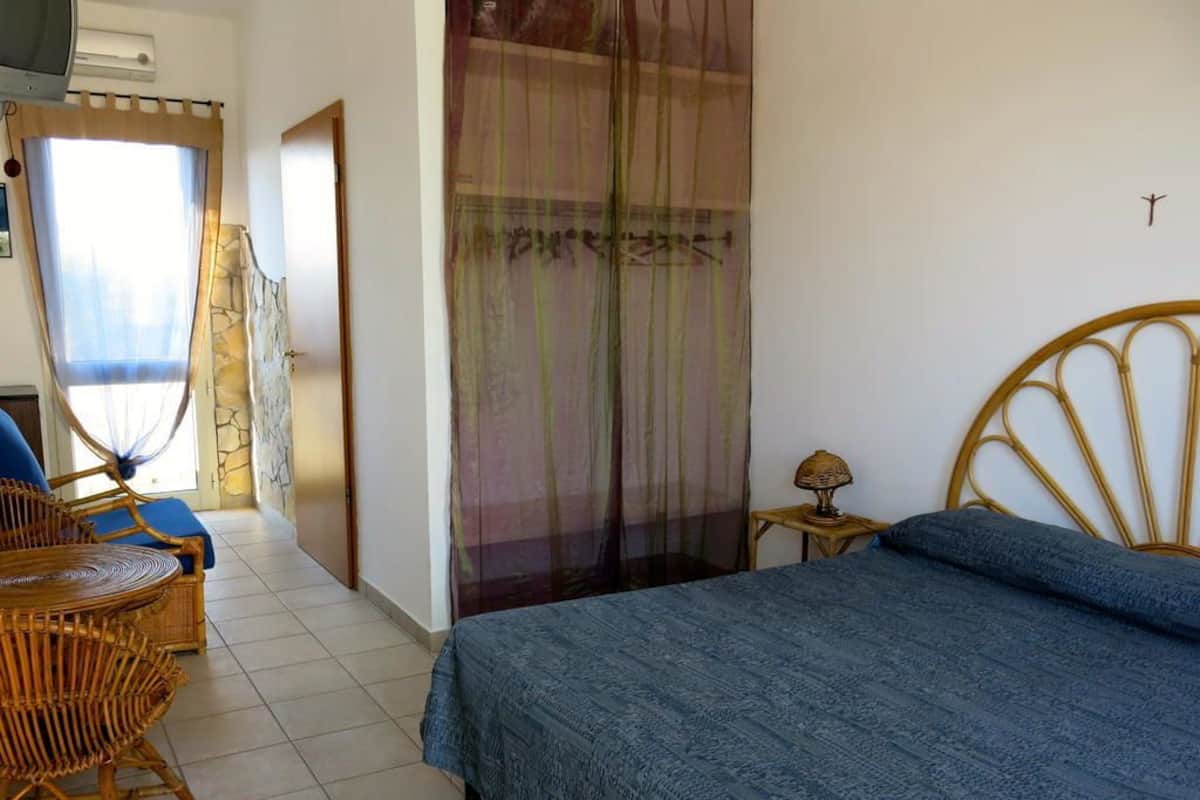 Una camera da letto con un letto, una sedia, un tavolino e una tenda.