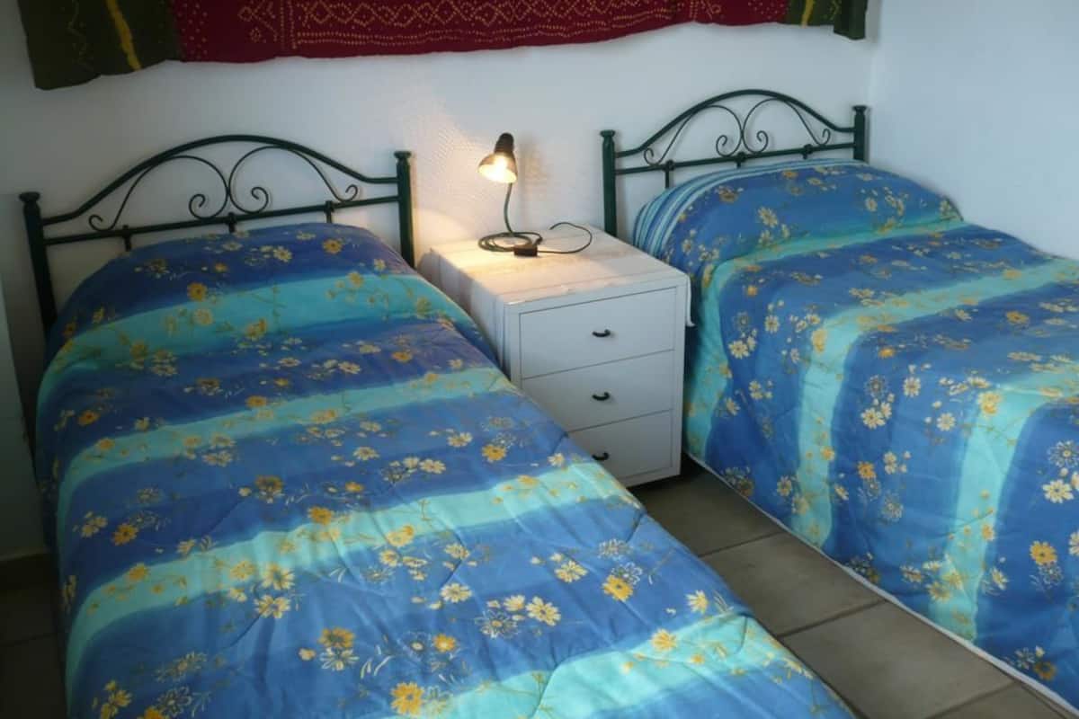 Una stanza con due letti, ognuno con una coperta a motivi floreali, un comodino con una lampada e un arazzo a parete.