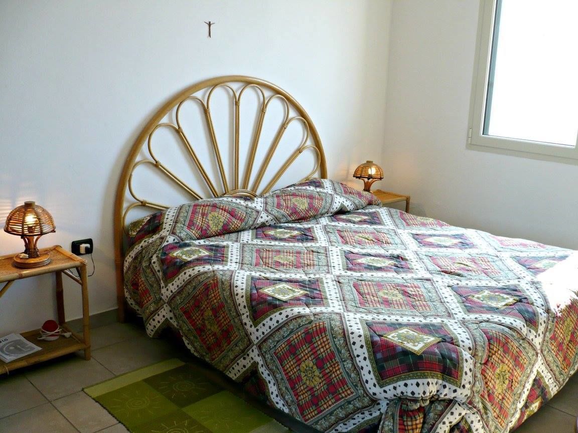 A bed with a patterned quilt, a wooden headboard, two bedside lamps, and a green rug.