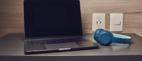 Una computadora portátil sobre un escritorio, con auriculares y un enchufe de corriente al fondo.