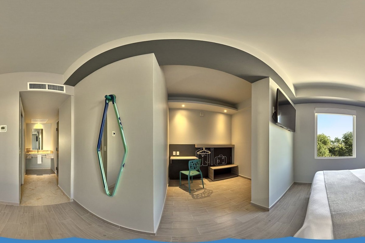 Habitación de hotel moderna con techo curvo, una cama grande, un escritorio y vistas al exterior.