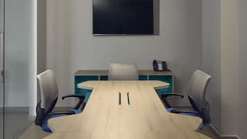 Uma sala de conferências com uma mesa comprida, quatro cadeiras, uma TV de tela plana na parede e uma luminária no teto.