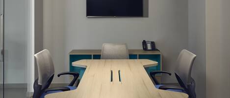 Un salón de conferencias con una mesa larga, cuatro sillas, un televisor de pantalla plana en la pared y una lámpara en el techo.